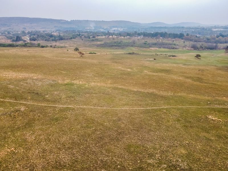 An aerial view of a large, open vacant residential plot featuring natural grassland and distant landscape views.