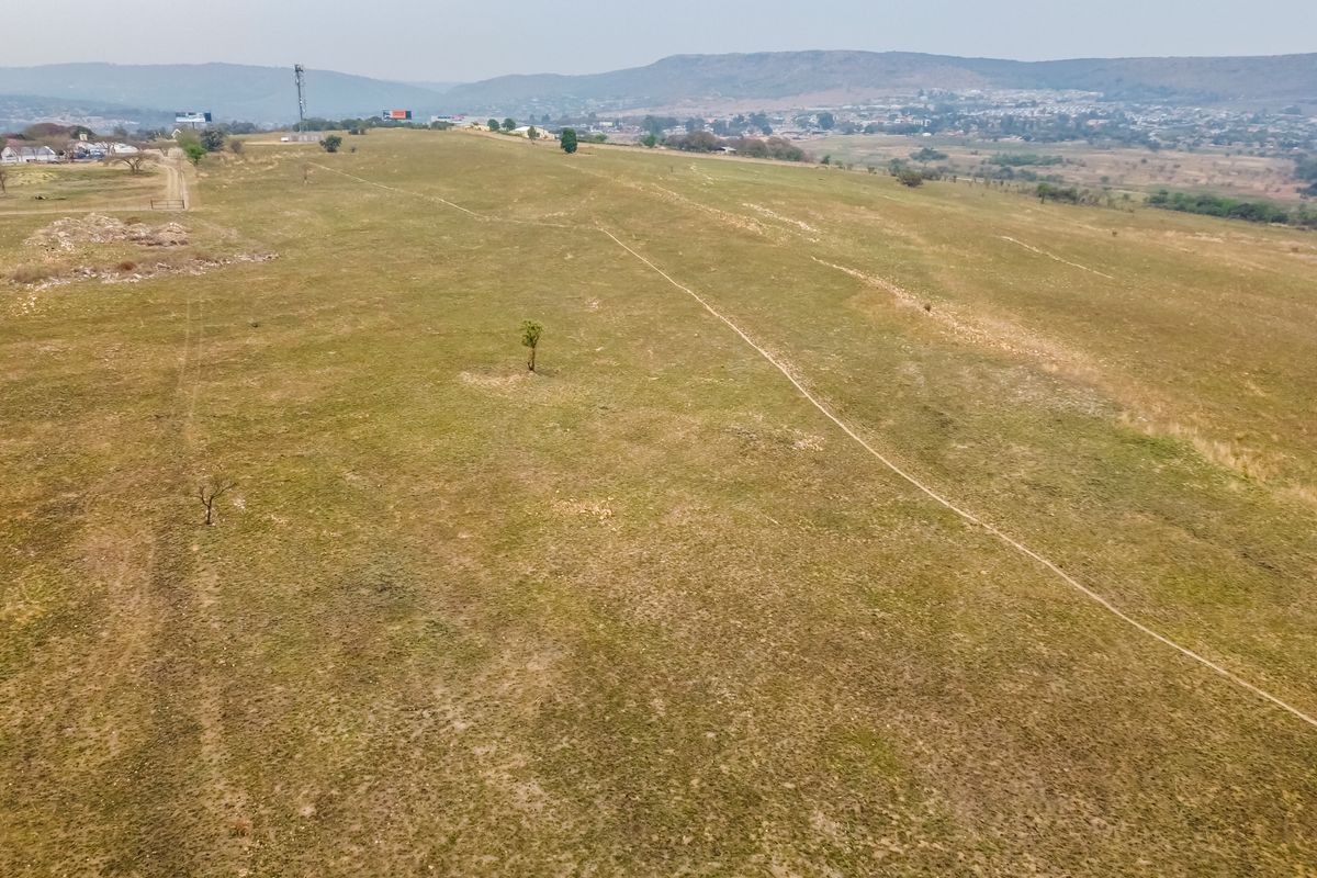 An aerial view of a large, undeveloped residential land parcel featuring open grassland and distant mountain views.