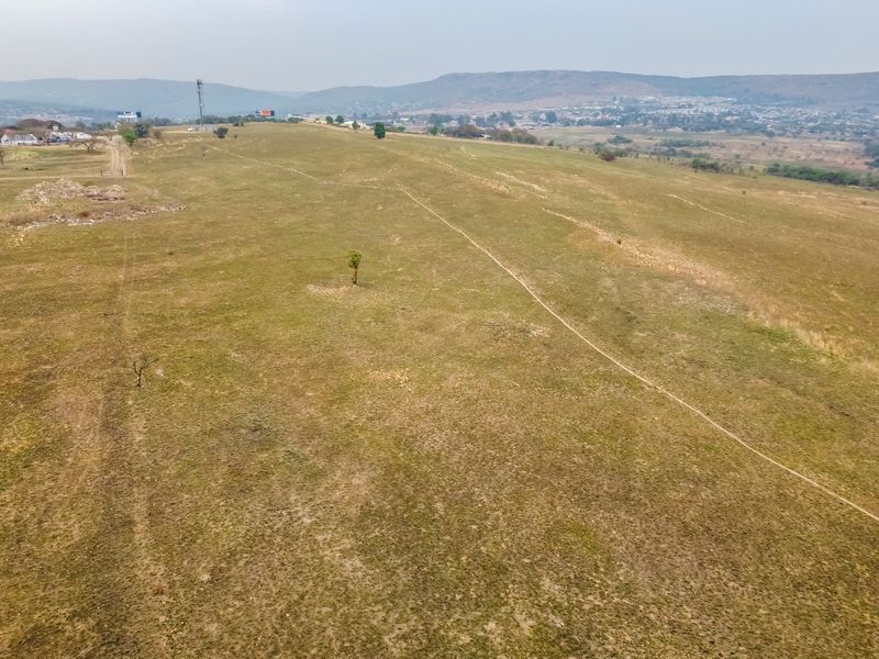 An aerial view of a large, undeveloped residential land parcel featuring open grassland and distant mountain views.