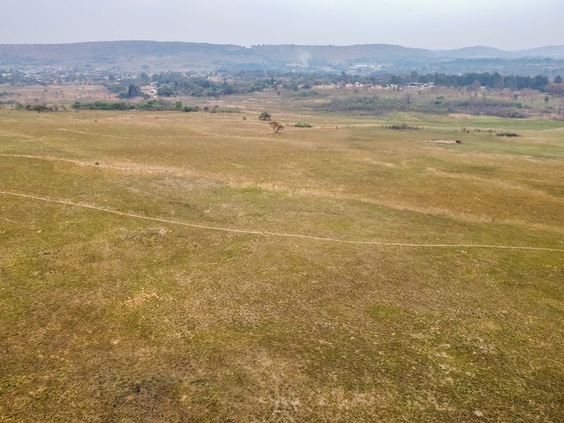 An aerial view of a large, open vacant residential plot featuring natural grassland and distant landscape views.