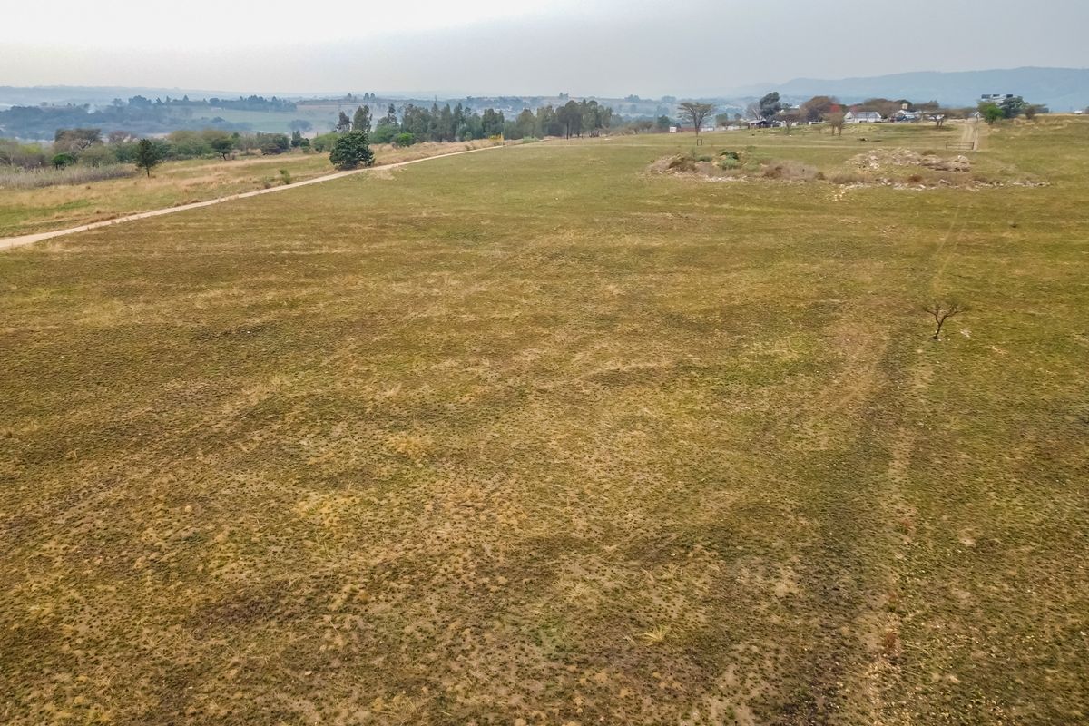 An aerial view of a large, undeveloped residential plot featuring open grassland and a dirt access track.