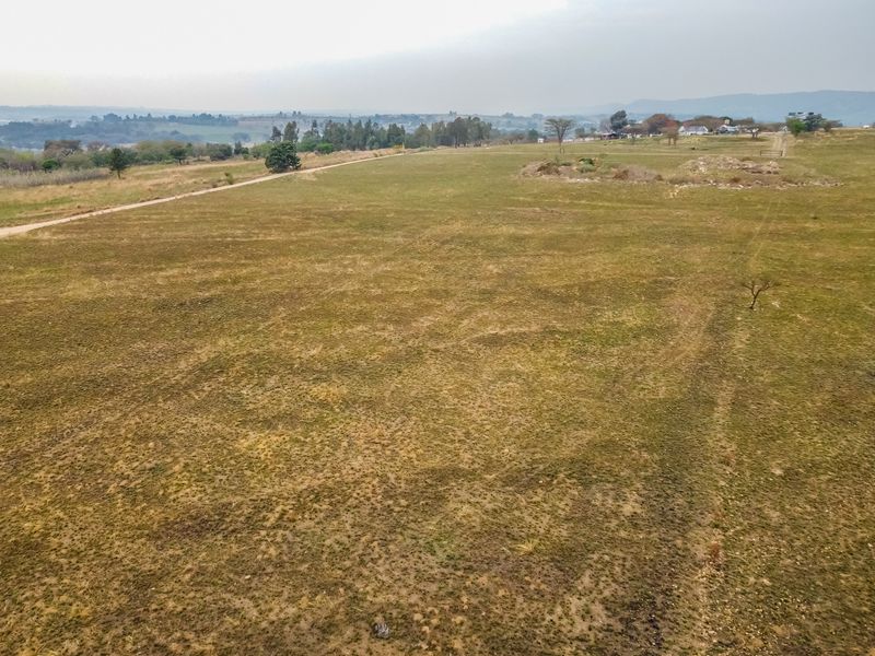 An aerial view of a large, undeveloped residential plot featuring open grassland and a dirt access track.