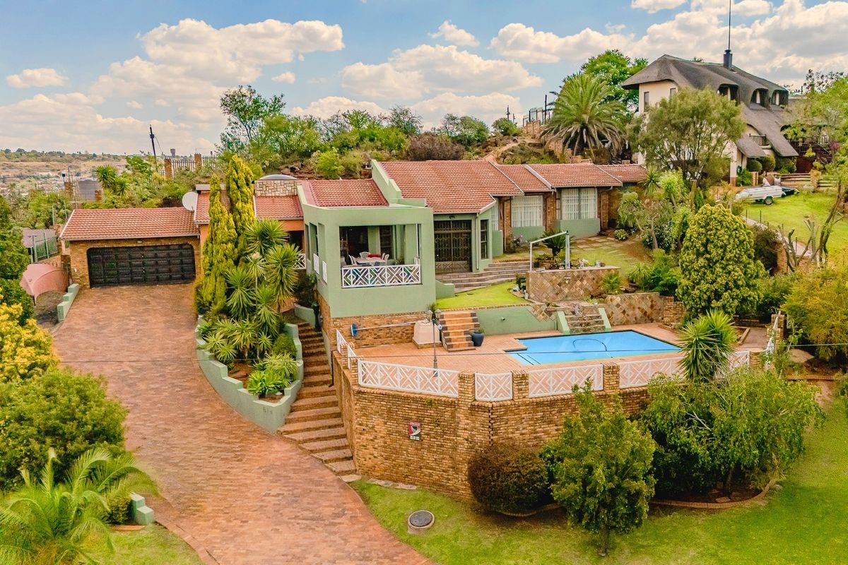 Aerial view of a multi-level residential property featuring a swimming pool, extensive brick paving, a double garage, and established garden landscaping.