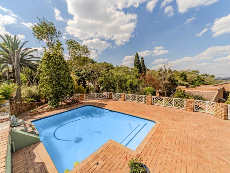 Outdoor pool area featuring a paved brick patio, brick boundary walls with lattice fencing, and established garden surroundings.