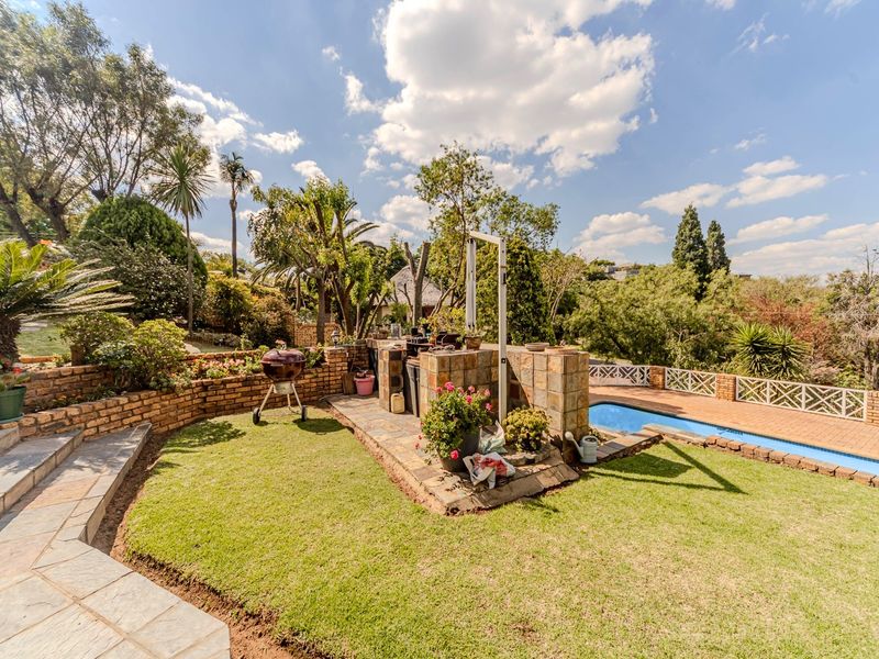 Outdoor entertainment area featuring a swimming pool, stone-paved patio, and a built-in brick braai station set within a landscaped garden.