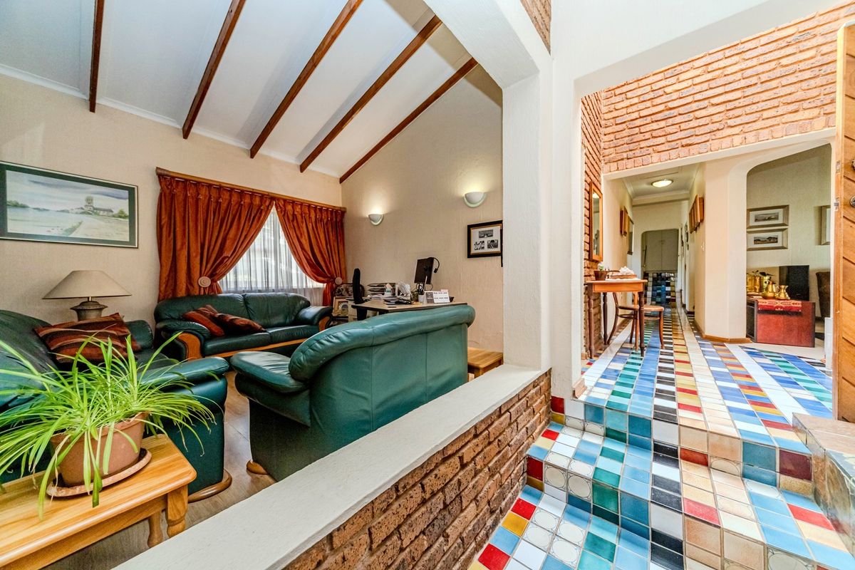 Spacious living area featuring exposed timber ceiling beams, a brick feature wall, and unique multi-colored tiled flooring leading into the hallway.