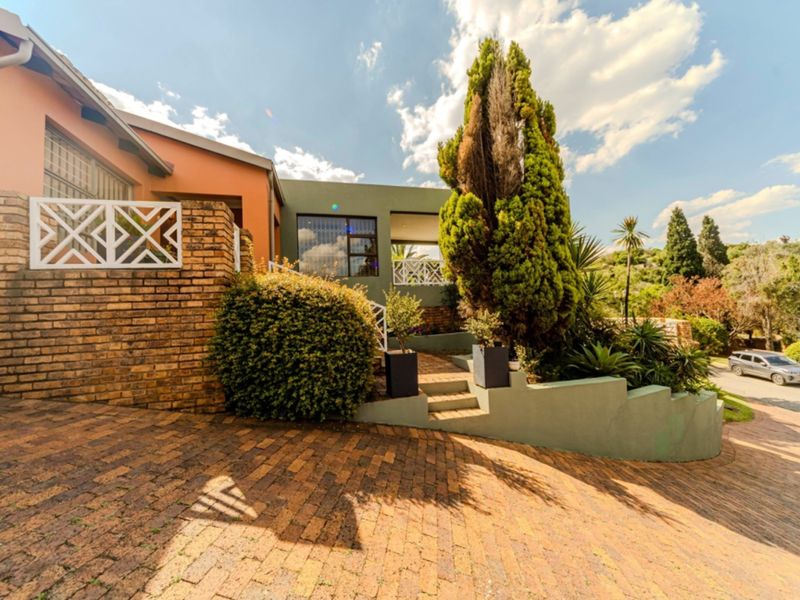 Front exterior view of the house featuring a brick driveway, landscaped retaining walls, concrete steps, and a covered patio area.