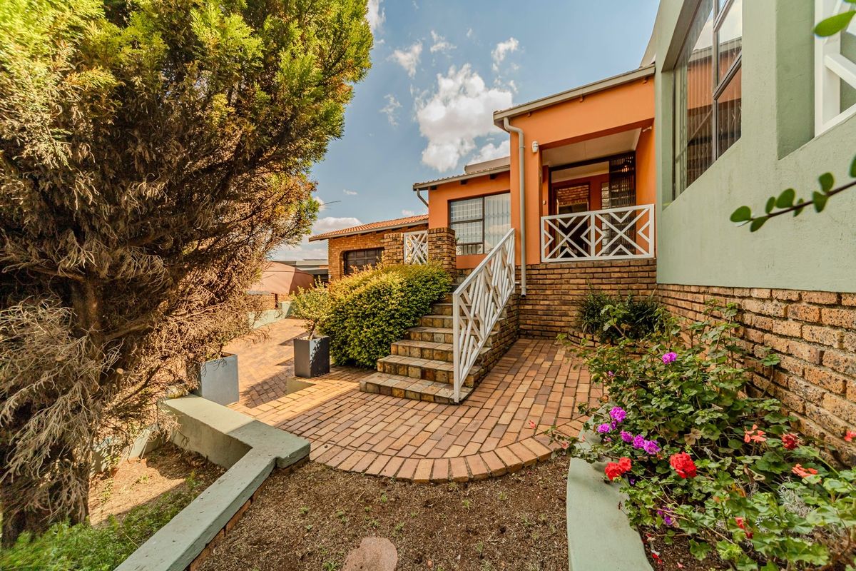 Rear exterior view featuring a brick-paved patio, staircase with metal railings, and established garden beds leading to a covered patio area.