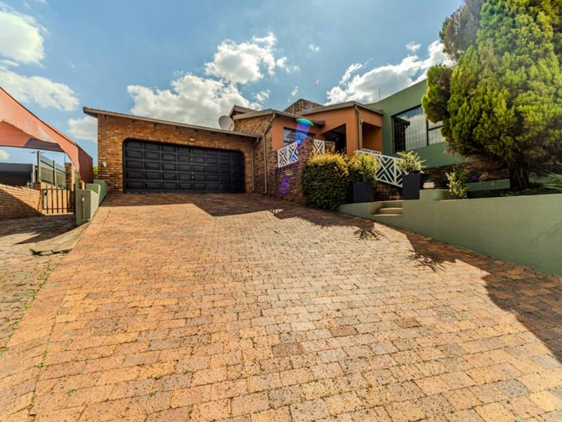 Front exterior view of the house featuring a brick paved driveway, double garage, and landscaped retaining walls leading to the main entrance.