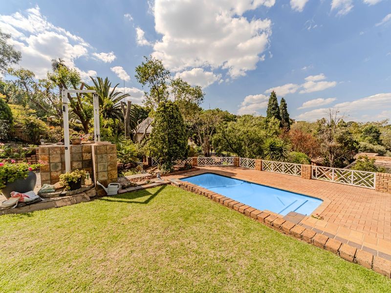 A well-maintained outdoor pool area featuring brick paving, a stone-clad feature wall, and decorative fencing set within a landscaped garden.