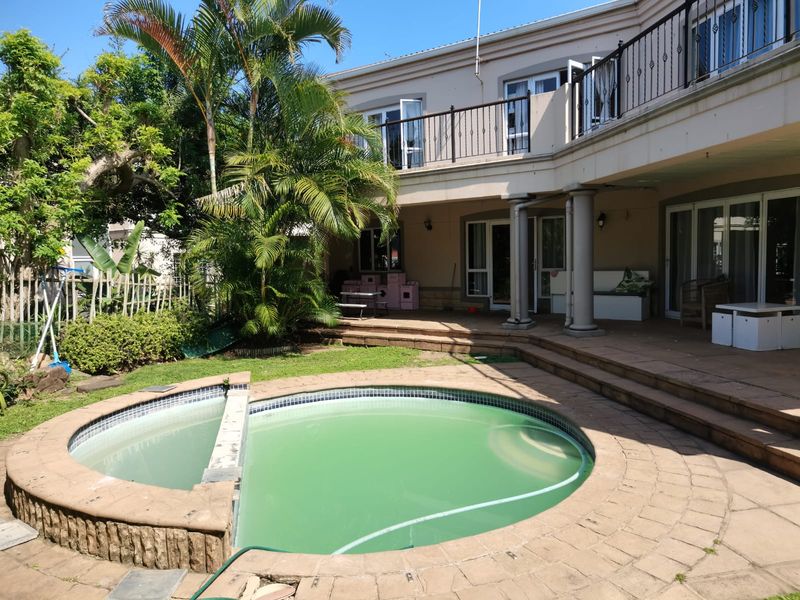 Rear exterior view featuring a raised patio, balcony with wrought iron railings, and a swimming pool requiring maintenance.