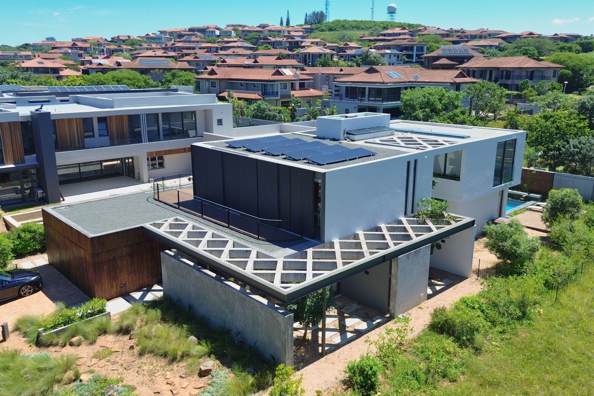 Aerial view of a modern architectural house featuring solar panels, a flat roof design, and integrated outdoor patio spaces within a residential estate.