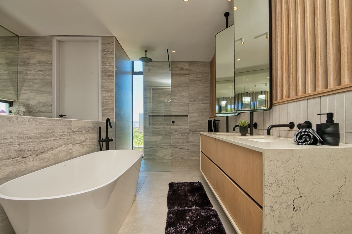 Modern bathroom featuring a freestanding bathtub, walk-in glass shower, double vanity with stone countertop, and contemporary matte black fixtures.