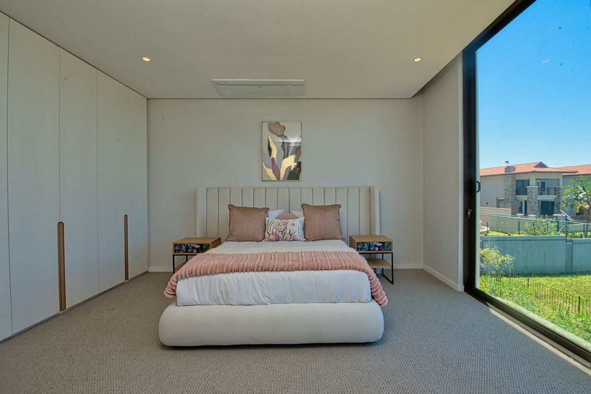 A modern, well-maintained bedroom featuring floor-to-ceiling built-in wardrobes, recessed ceiling lighting, a ducted air conditioning unit, and large sliding glass doors leading outdoors.