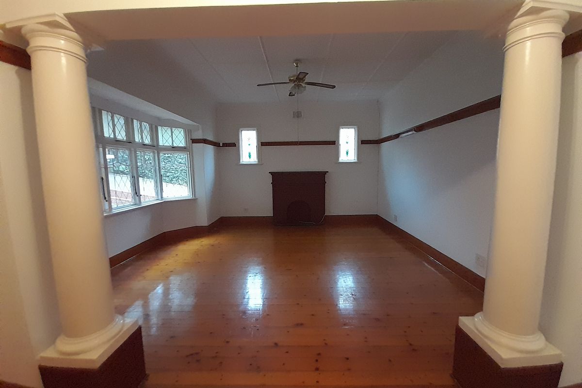 Spacious living room featuring polished hardwood floors, decorative columns, a classic fireplace mantel, and a bright bay window.
