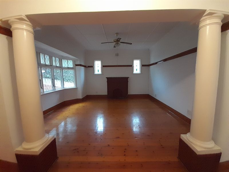 Spacious living room featuring polished hardwood floors, decorative columns, a classic fireplace mantel, and a bright bay window.