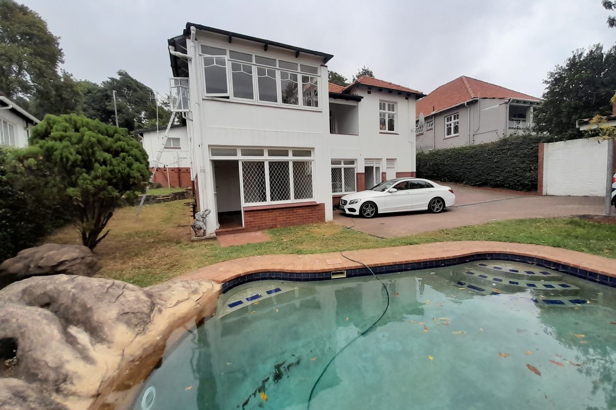 Rear view of a multi-level house featuring a swimming pool with rock landscaping, a paved driveway, and an enclosed upper-level balcony.