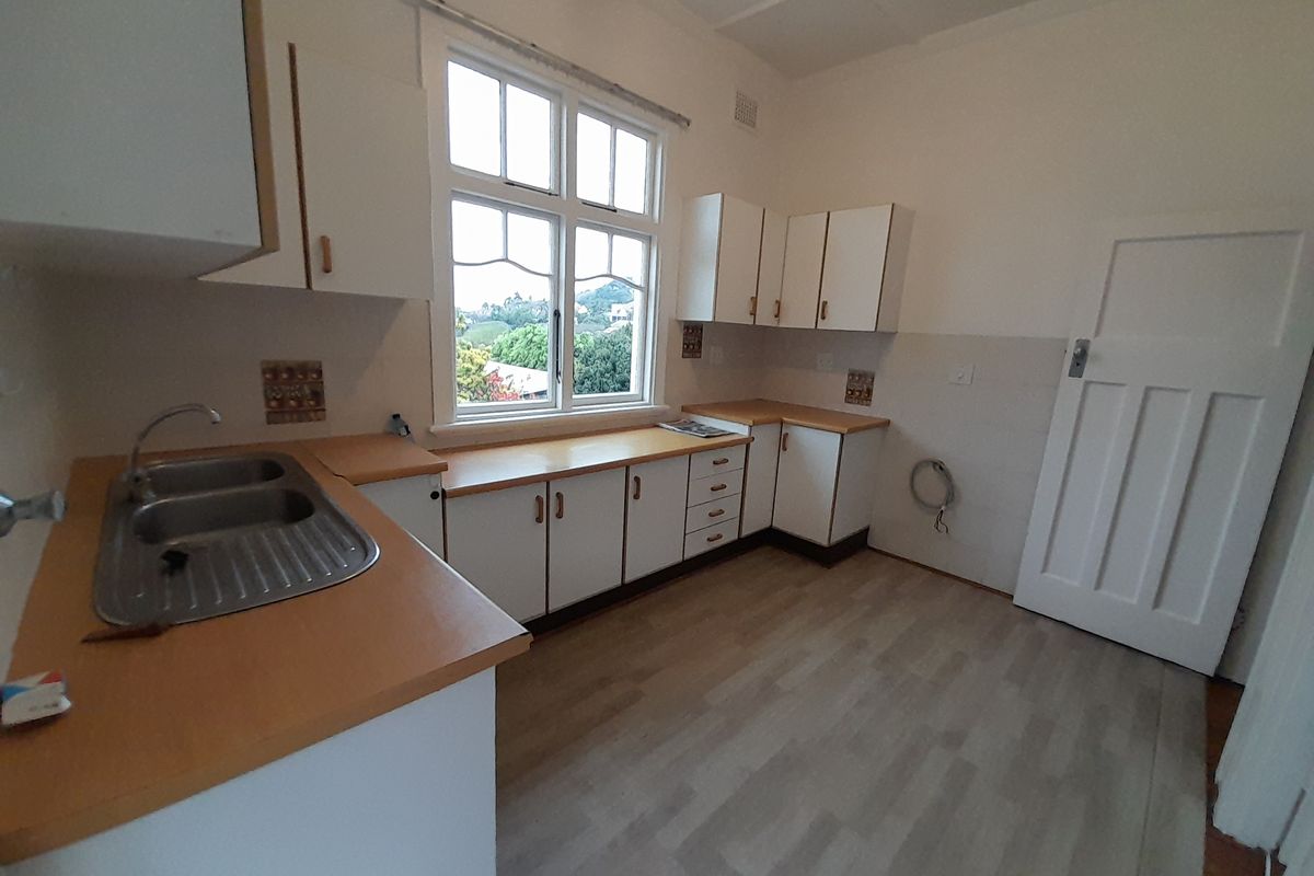 A functional, empty kitchen featuring white cabinetry, laminate countertops, a double bowl sink, and a large window providing natural light.