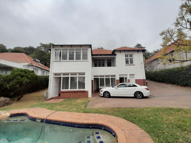 Rear view of a two-story house featuring a swimming pool, brick-paved driveway, and traditional multi-pane windows under a tiled roof.
