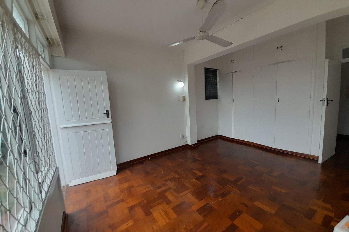 A spacious, empty bedroom featuring classic parquet flooring, built-in storage cupboards, and a ceiling fan, offering a clean canvas for personalization.