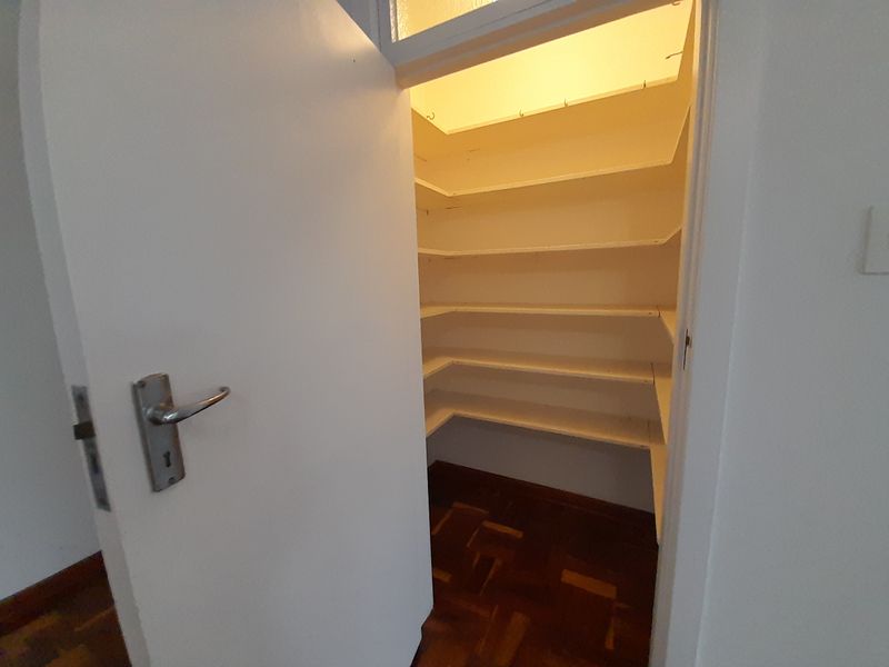 A walk-in pantry or scullery area featuring built-in white shelving and traditional parquet flooring.