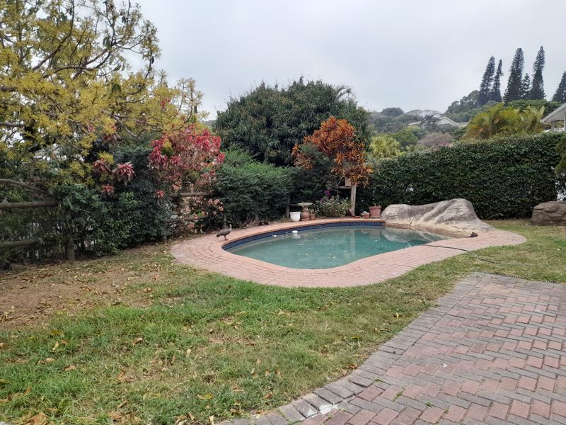 Outdoor pool area featuring a swimming pool with brick coping, surrounding brick paving, and established garden landscaping.