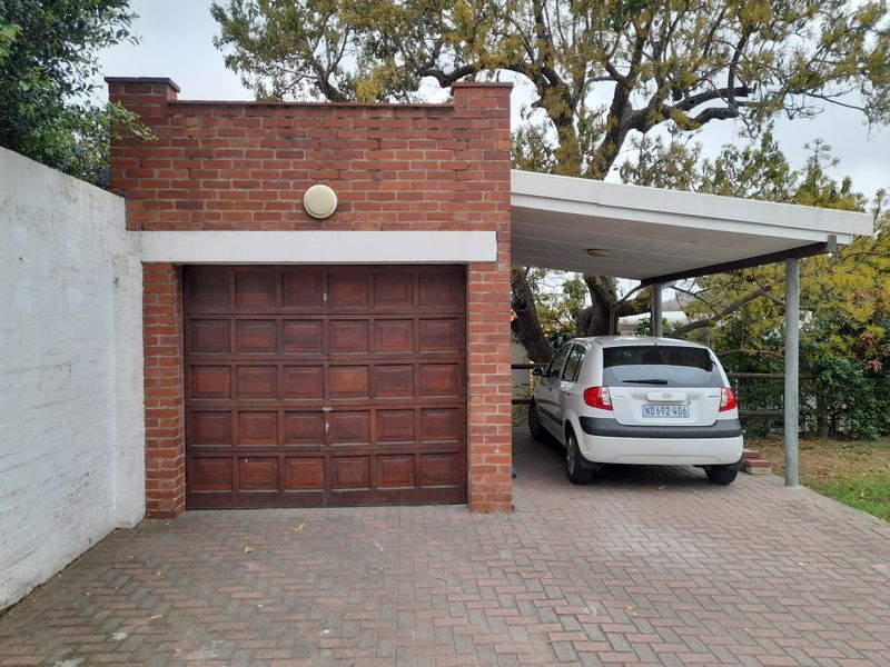 A single brick garage featuring a wooden door, complemented by an adjacent covered carport and a paved driveway area.