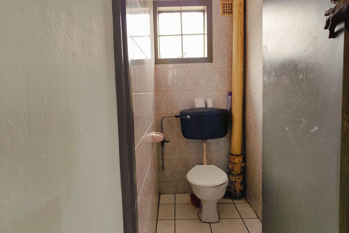 A compact, dated bathroom featuring a standard toilet, tiled walls and flooring, and an exposed vertical plumbing pipe.