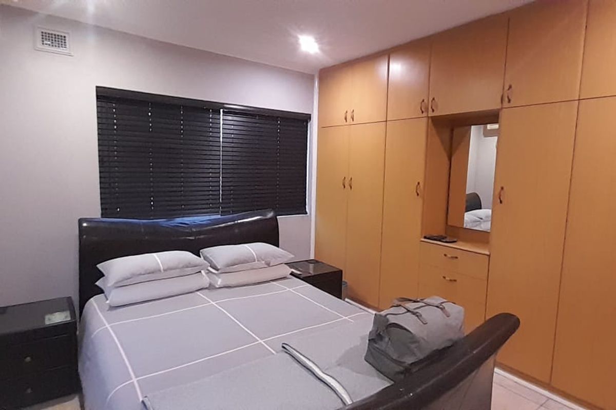 A bedroom featuring extensive floor-to-ceiling built-in wooden cabinetry with integrated vanity and dark window blinds.