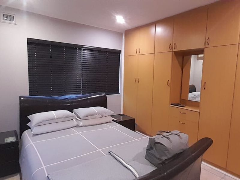 A functional bedroom featuring extensive built-in wooden cabinetry, tiled flooring, and venetian blinds for privacy.