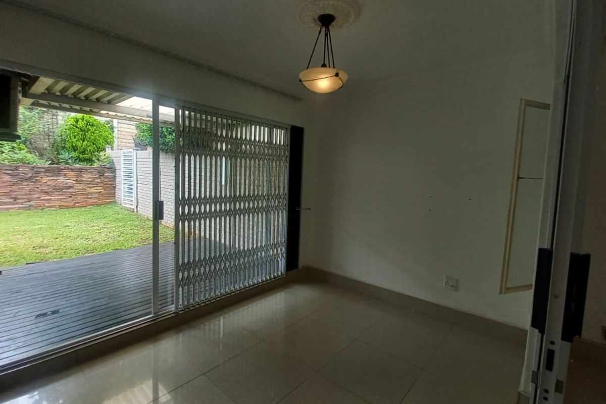 An empty living room featuring tiled flooring and a sliding glass door with a security gate, providing direct access to a rear patio and garden.
