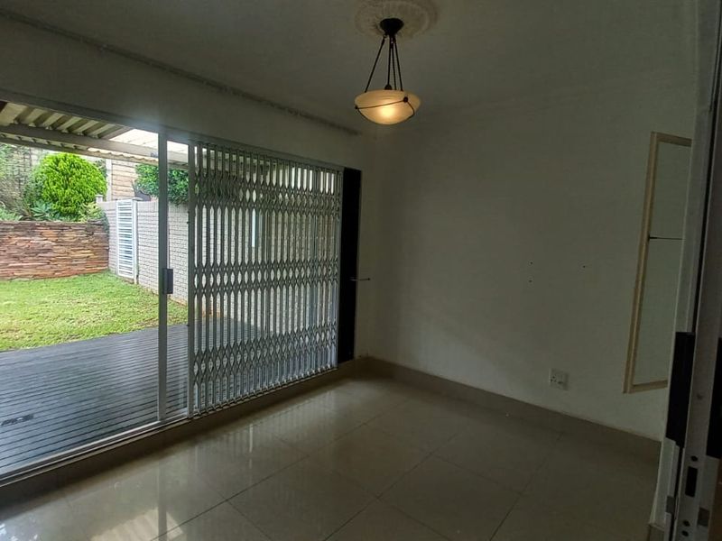 An empty living room featuring tiled flooring and a sliding glass door with a security gate, providing direct access to a rear patio and garden.