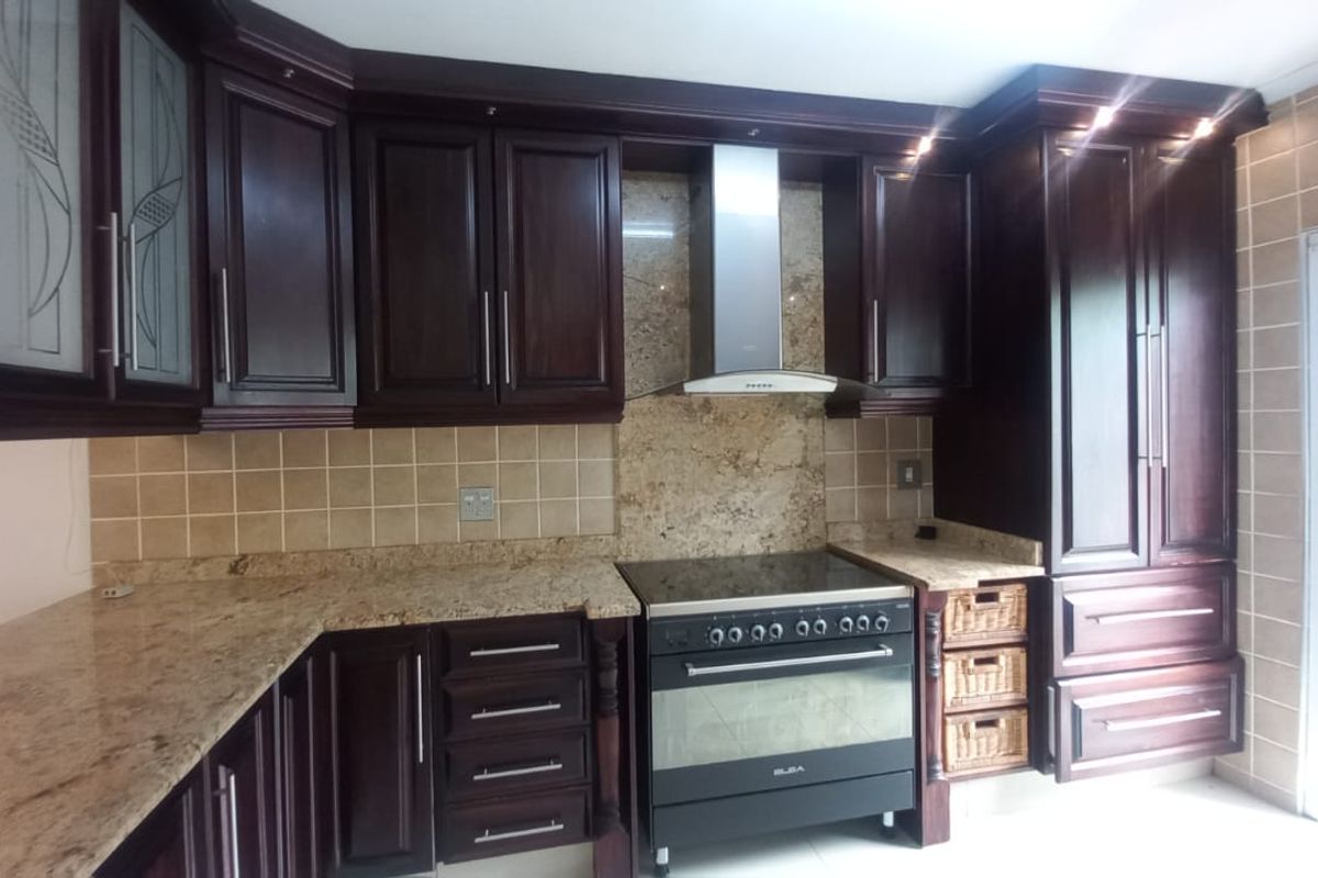 A well-maintained kitchen featuring dark wood cabinetry, granite countertops, a tiled backsplash, and a stainless steel extractor fan with a freestanding oven.
