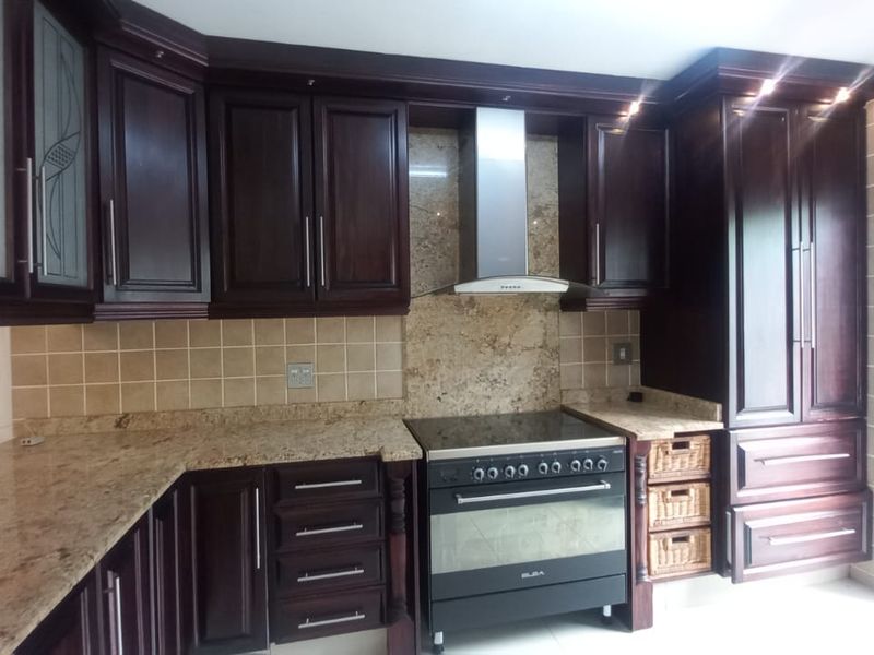 A well-maintained kitchen featuring dark wood cabinetry, granite countertops, a tiled backsplash, and a stainless steel extractor fan with a freestanding oven.