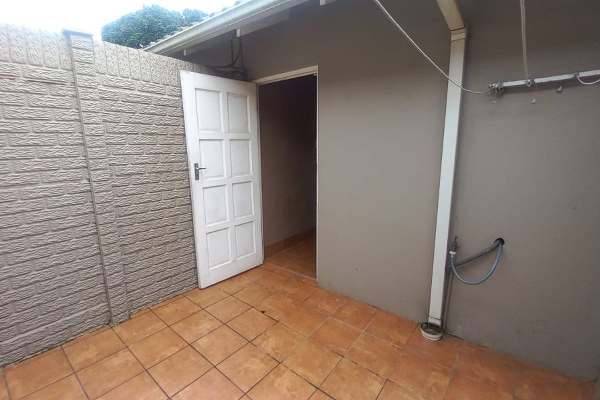 A functional rear courtyard area featuring tiled flooring, a brick boundary wall, and convenient outdoor utility fixtures including a tap and clothesline.