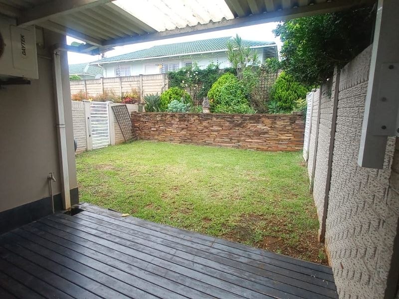 A covered timber deck patio overlooking a private garden with a stone-clad retaining wall and secure boundary fencing.