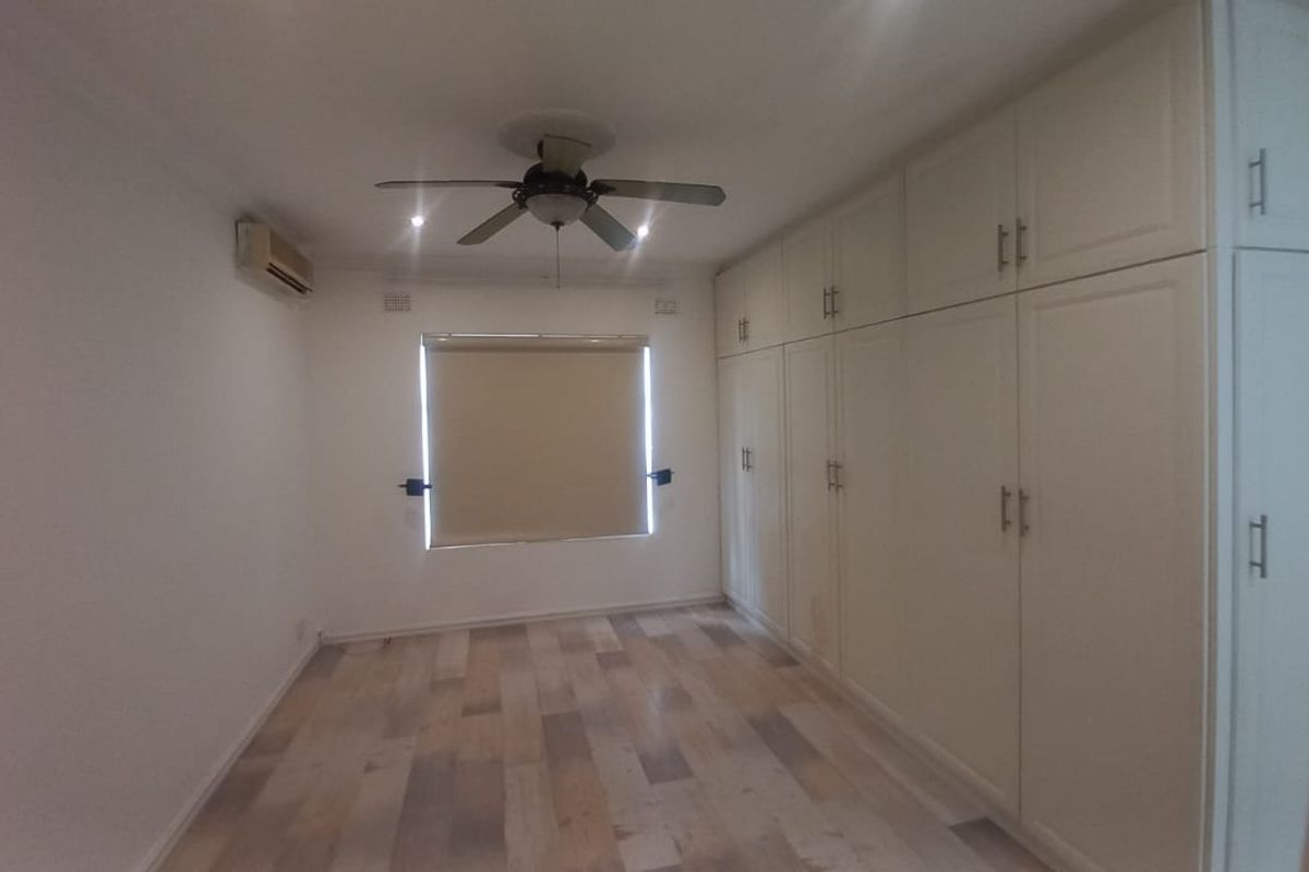 Spacious bedroom featuring extensive built-in cupboards, laminate flooring, a ceiling fan, and an air conditioning unit.