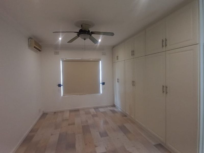 Spacious bedroom featuring extensive built-in cupboards, laminate flooring, a ceiling fan, and an air conditioning unit.
