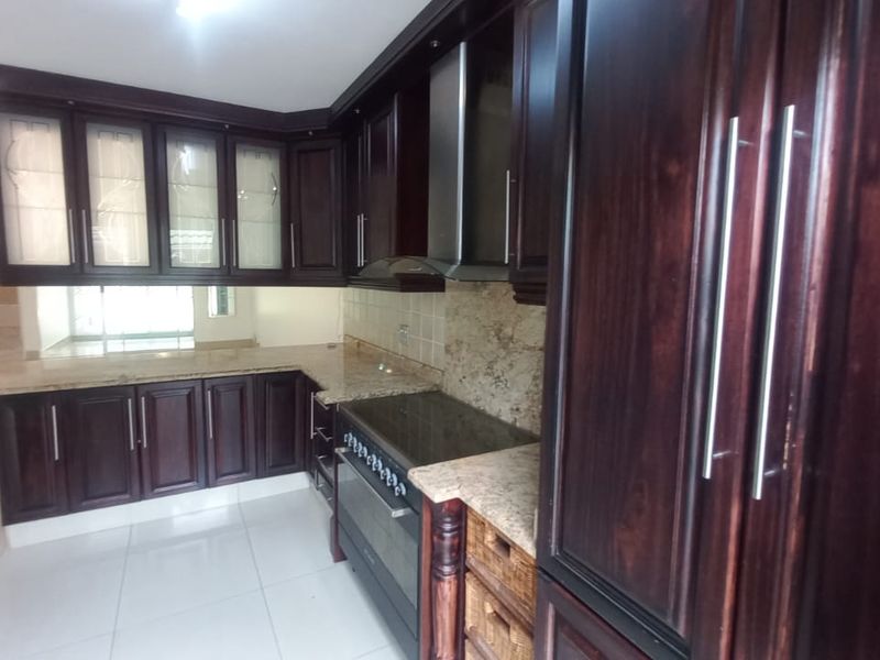 A spacious kitchen featuring dark wood cabinetry, granite countertops, built-in oven, and extractor fan, with neutral tiled flooring throughout.