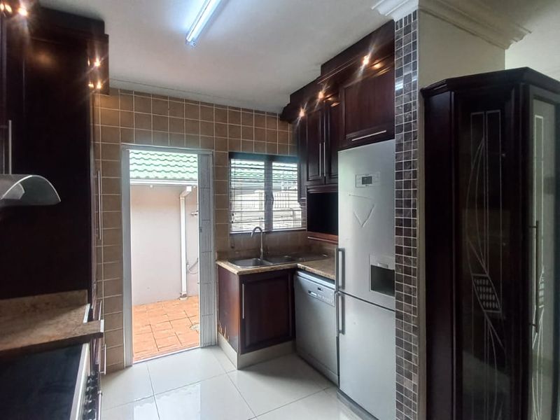 A functional kitchen featuring dark wood cabinetry, granite countertops, tiled backsplash, and direct access to an outdoor patio area.