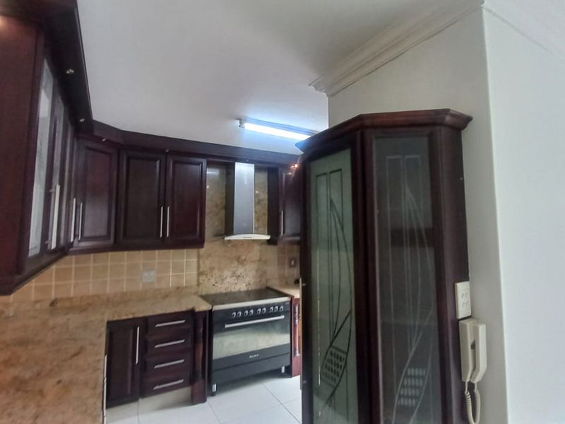 A functional kitchen featuring dark wood cabinetry, granite countertops, a tiled backsplash, and a stainless steel extractor fan with a freestanding oven.