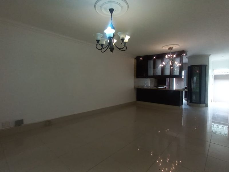 Spacious open-plan living and kitchen area featuring tiled flooring, decorative ceiling roses with chandeliers, and a built-in kitchen breakfast bar.