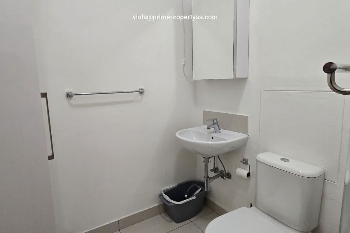 A compact bathroom featuring a wall-mounted basin, a standard toilet, and a glass-enclosed shower area with tiled flooring.