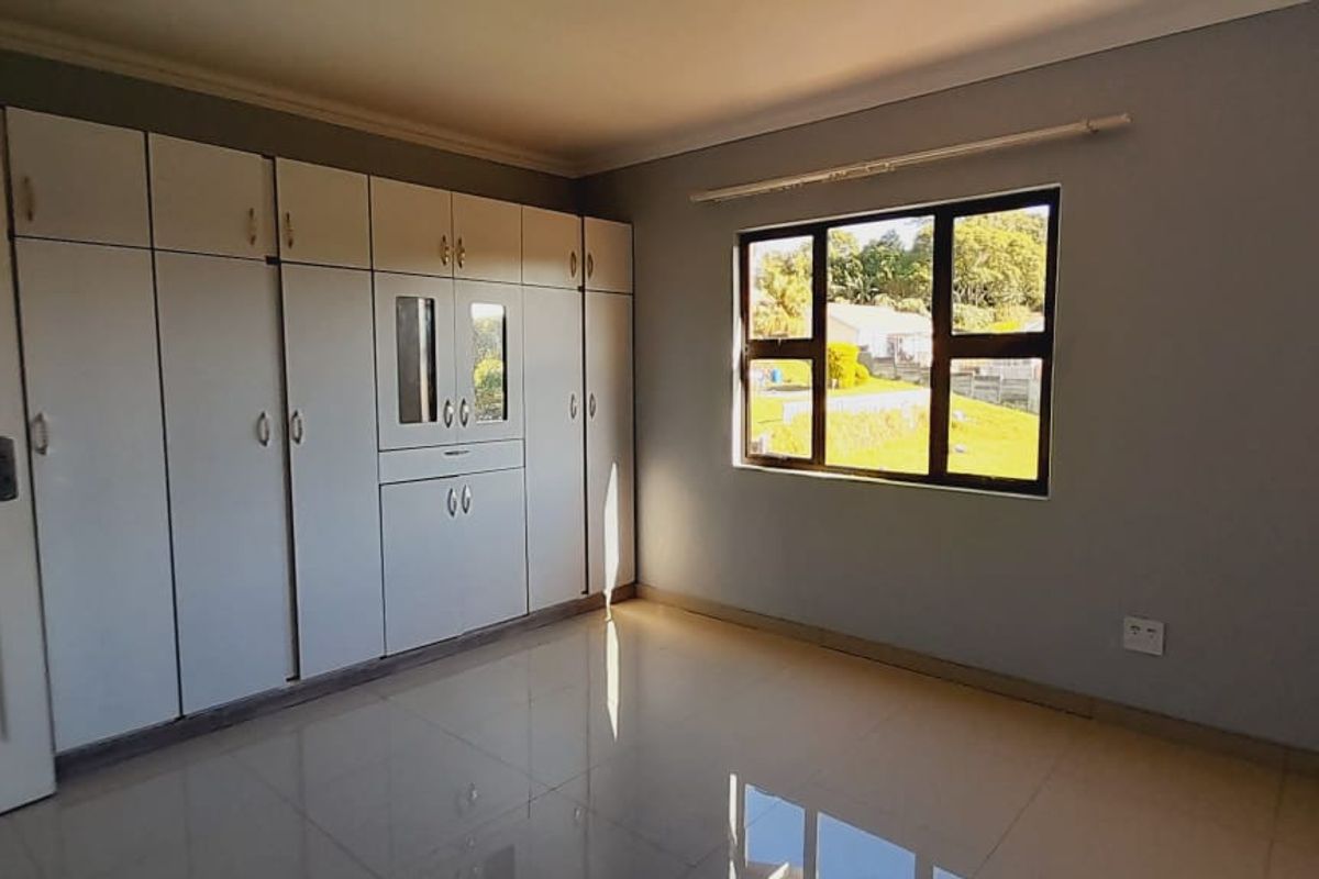 A bright bedroom featuring built-in cupboards, tiled flooring, and a window providing natural light.
