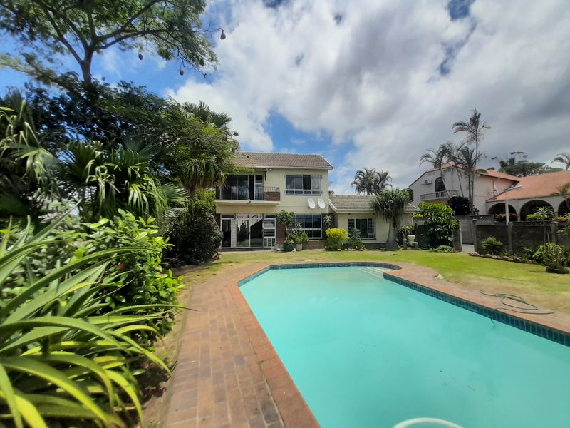 Rear view of the cluster property featuring a swimming pool, paved surround, and established garden area with a two-story building facade.