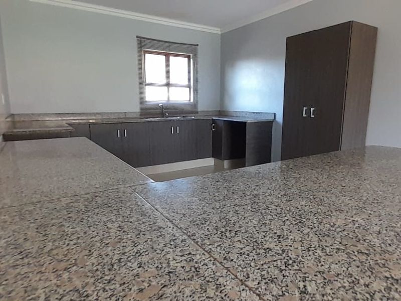 A functional kitchen featuring granite countertops, dark cabinetry, and a built-in pantry cupboard, offering ample workspace and storage.