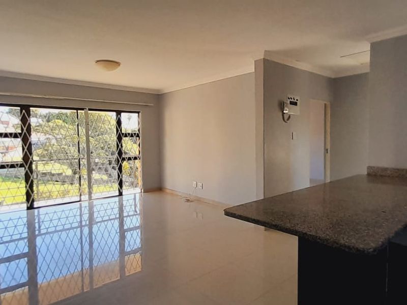 Spacious open-plan living area featuring polished tile flooring, a breakfast counter, and large sliding doors with security gates leading to the exterior.