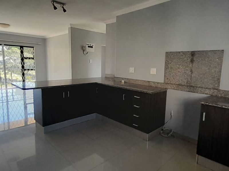 Open plan kitchen area featuring dark cabinetry, granite countertops, and tiled flooring, flowing into a spacious living area with large sliding doors.