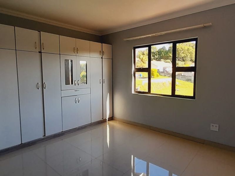 A bright bedroom featuring built-in cupboards, tiled flooring, and a window providing natural light.