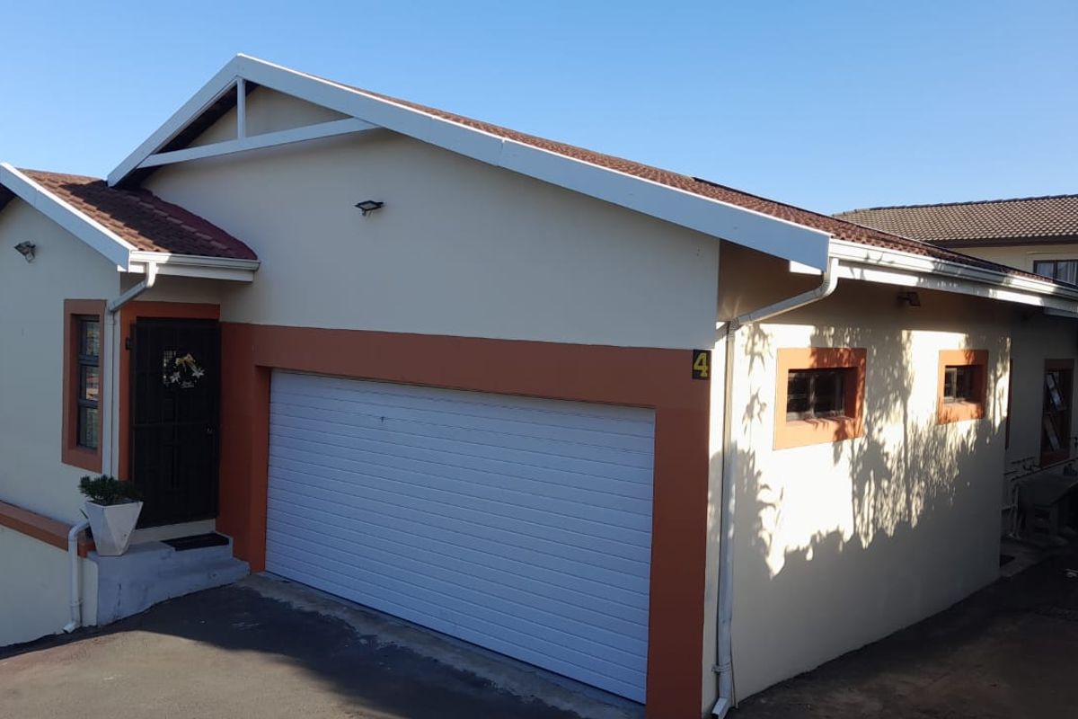 Front exterior view of the cluster home featuring a double garage, paved driveway, and neutral facade with contrasting trim.